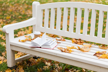 Image showing open book and coffee cup on bench in autumn park