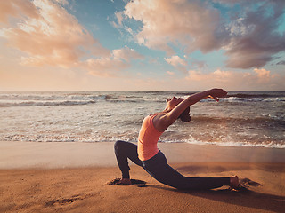 Image showing Sporty fit woman practices yoga Anjaneyasana at beach on sunset