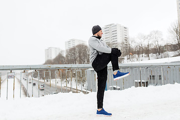 Image showing man exercising and stretching leg on winter bridge