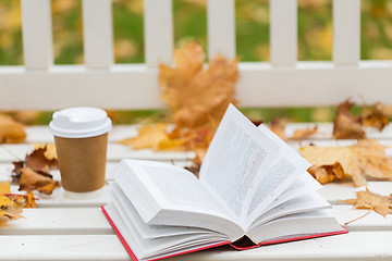 Image showing open book and coffee cup on bench in autumn park