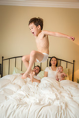 Image showing Mixed Race Chinese and Caucasian Boy Jumping In Bed with His Fam