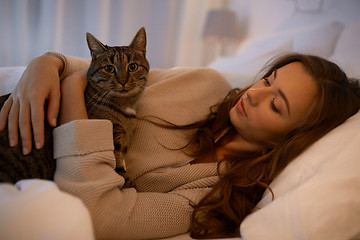 Image showing happy young woman with cat lying in bed at home