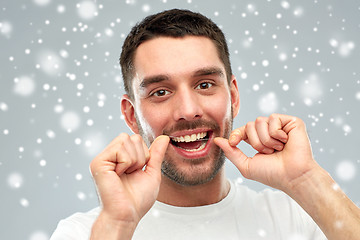 Image showing man with dental floss cleaning teeth over snow