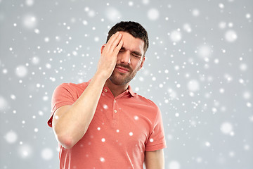 Image showing unhappy man suffering from head ache over snow