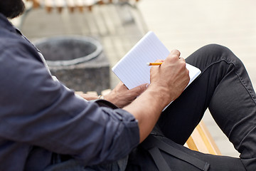 Image showing close up of man writing to notebook on city street