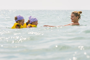 Image showing Mom floats in the sea with two small daughters in swimming vests