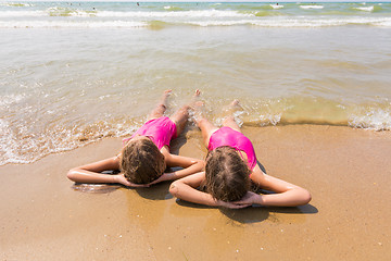 Image showing Two girls lie on your back on the sandy beach and looking at sea