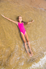 Image showing Seven-year girl lies on her back in the water on the sandy beach