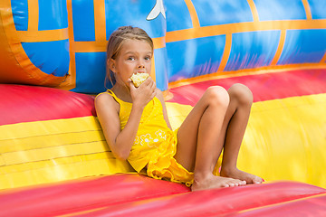 Image showing Girl sits at the entrance to an inflatable trampoline and eating an apple