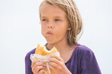 Image showing A hungry girl with an appetite chews delicious cake on the beach