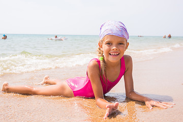 Image showing Happy girl lying on the sand near the water on the beach and smiling happily looks into the frame