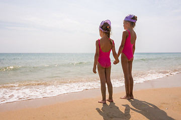 Image showing Two girls in bathing suits standing on the beach and look at the horizon