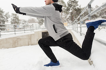 Image showing sports man stretching leg at fence in winter