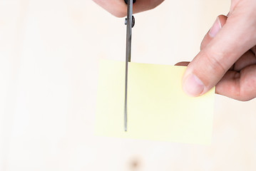 Image showing A man is cutting a sheet of yellow paper using metallic scissors