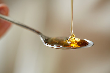 Image showing close up of honey pouring to teaspoon