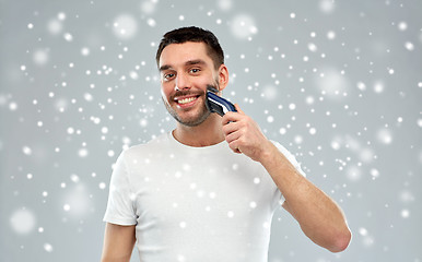 Image showing smiling man shaving beard with trimmer over snow