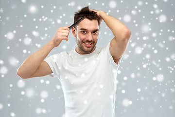 Image showing happy man brushing hair with comb over snow