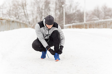 Image showing man with earphones tying sports shoe in winter