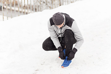 Image showing man with earphones tying sports shoe in winter