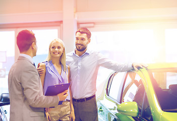 Image showing happy couple with car dealer in auto show or salon