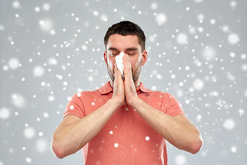 Image showing sick man with paper wipe blowing nose over snow