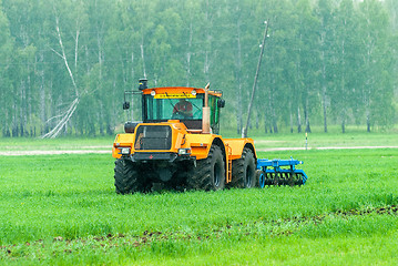 Image showing Tractor operator plows the site in rain