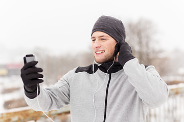 Image showing happy man with earphones and smartphone in winter