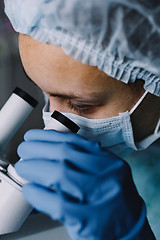 Image showing Young scientist in uniform looking at microscope