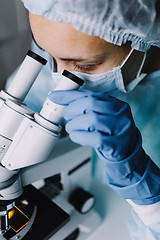 Image showing Young scientist in uniform looking at microscope