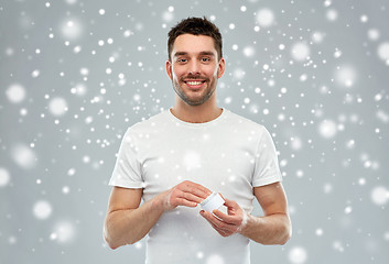 Image showing happy young man with cream jar over snow