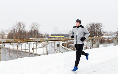 Image showing man in earphones running along winter bridge