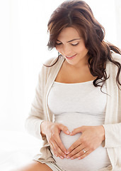 Image showing happy pregnant woman making heart gesture at home