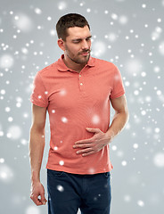 Image showing unhappy man suffering from stomach ache over snow