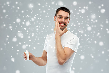 Image showing happy young man applying cream or lotion to face