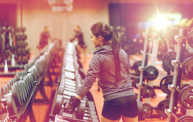 Image showing young woman choosing dumbbells in gym