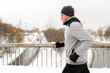 Image showing man in earphones running along winter bridge