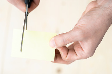 Image showing A man is cutting a sheet of yellow paper using metallic scissors