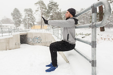 Image showing sports man doing squats at fence in winter