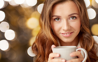 Image showing close up of happy woman with tea cup over lights