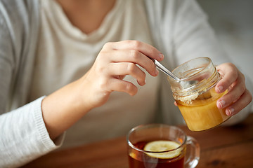 Image showing close up of woman adding honey to tea with lemon