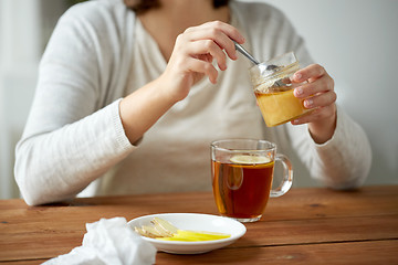 Image showing close up of woman adding honey to tea with lemon