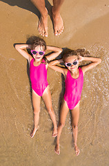 Image showing Two girls lie on his back on the surf of the sea sandy beach, there are a number of adult human foot