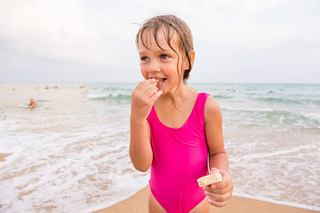 Image showing The girl in the pink bathing suit standing on the beach and eating waffle