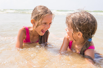 Image showing Two girls lying in the shallow water and have fun looking at each other