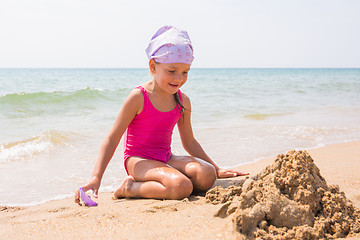 Image showing Girl happily looks at the sand pit dug up, sitting on the beach