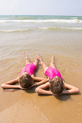 Image showing Two girls lie on your back on the sandy beach halfway in the wate