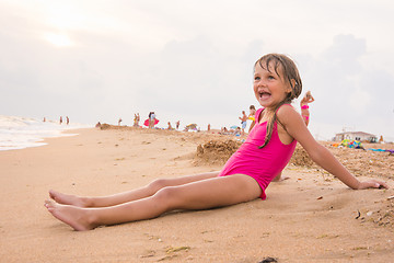 Image showing Five-year girl sits on the beach in the evening sea coast on a cloudy day