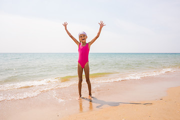 Image showing Happy girl lifted her arms up on the sandy shore of the sea