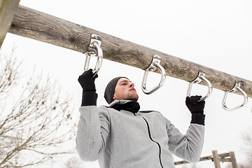 Image showing young man exercising on horizontal bar in winter