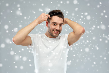 Image showing happy man brushing hair with comb over snow